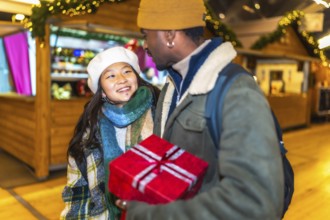 Young multiethnic couple holding a christmas gift, enjoying christmastime at a christmas market