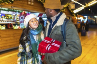 Young multiethnic couple joyfully holding a beautifully wrapped christmas gift while enjoying the