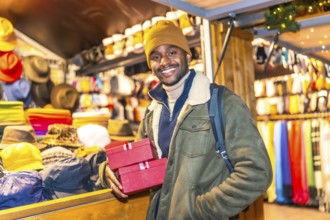 Young man holding christmas presents at a christmas market stall, enjoying the festive atmosphere