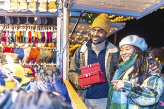 Young multiethnic couple enjoying christmas shopping at a decorated christmas market, holding red