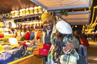 Happy multiethnic couple exchanging christmas presents at a stall in a christmas market at night