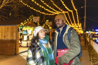 Young multiethnic couple walking and enjoying christmastime at a decorated outdoor market with