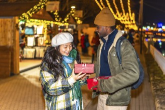 Happy multiethnic couple exchanging christmas gifts at a festively decorated christmas market,