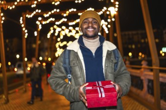 Smiling tourist holding christmas present while enjoying winter holidays in decorated city