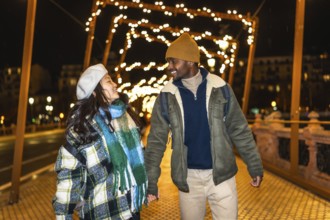 Young multiethnic tourists couple holding hands, enjoying christmas lights decoration at night