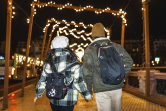 Multiethnic couple walking on bridge at night, holding hands and enjoying christmas lights