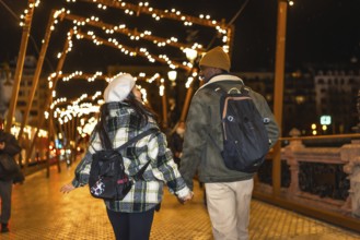 Young multiethnic couple walking on bridge with christmas lights, enjoying winter holidays