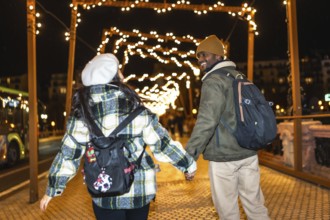 Multiethnic couple walking hand in hand under glowing christmas lights, enjoying a magical night