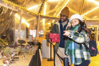 Happy multiethnic couple holding christmas gifts and admiring a nativity scene at a christmas