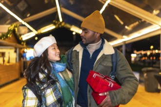 Young multiethnic couple exchanging christmas gifts and enjoying christmas time at a christmas