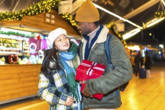 Happy multiethnic couple holding a christmas present, enjoying christmas time at a christmas market
