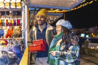 Young multiethnic couple enjoying christmas shopping at a decorated christmas market, holding red