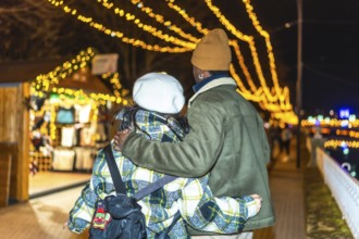 Multiethnic couple strolling through a beautifully decorated outdoor christmas market, embracing