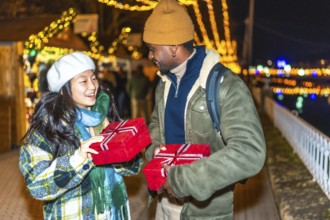 Young multiethnic couple exchanging christmas gifts at a christmas market, enjoying the festive