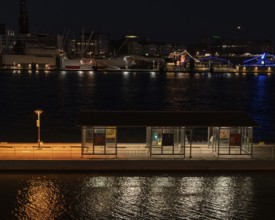 Night shot of a pontoon with bus shelter at the theatre on the Elbe with a view of the lighting of