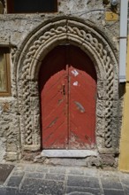 Red door with Romanesque arch and decorative stone carvings in an old façade, Turkish Quarter,