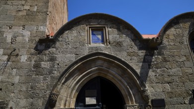 Kasteliani Public Library, Italian coat of arms, Historic stone gate under a clear blue sky, Rhodes