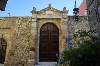 Gate of a synagogue, Massive wooden door in an old stone wall under a blue sky with blooming