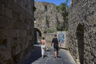 Saint John's Tor, Narrow alleyway lined with old walls with wall art and walkers in sunny weather,
