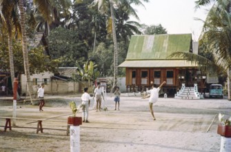 Traditional village houses in coconut palm trees, boys and young men playing Sepak Takraw foot