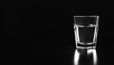 Clear Drinking Container Placed On A Dark Surface. Transparent Glass Resting On A Black Background.