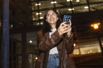 Young woman happily smiling and looking up while using her smartphone and wireless earbuds at