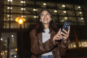 Young woman smiling and looking up, listening to music with wireless earbuds and using a smartphone