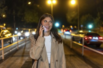 Young adult woman enjoying a happy conversation on smartphone while walking on a city street at