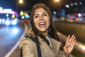 Young woman smiling and taking a nighttime selfie on a vibrant city street, capturing candid joy