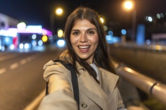Young woman smiling and taking a selfie on a lively city night, bokeh street lights and light