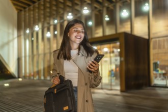 Young businesswoman smiling while checking her smartphone, holding a briefcase and walking alone on