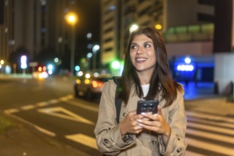Young woman smiling and looking away while using a mobile phone on a pedestrian crossing, waiting