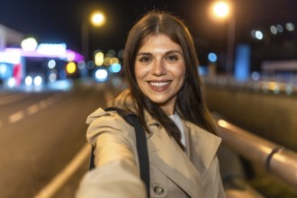 Young woman smiling and holding a smartphone, capturing a selfie portrait outdoors in an urban