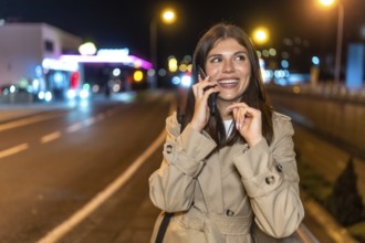 Young woman in a trench coat smiling and laughing while talking on her smartphone during an
