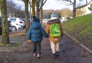 Two young children holding hands and walking home from school on a chilly winter day in bayonne,