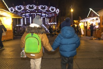 Two young boys holding hands are walking through a christmas market at night in bayonne, france,