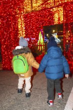 Two young boys holding hands walking through a christmas light display in bayonne, france at night