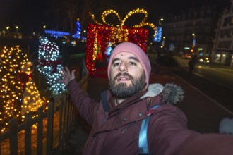 Bearded tourist taking a selfie with christmas lights and decorations in bayonne, france, at night