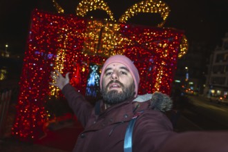 Bearded man taking a selfie in front of giant luminous christmas gift box in bayonne, france