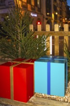 Large red and blue christmas presents sit on a wooden platform, adorned with fir branches, creating