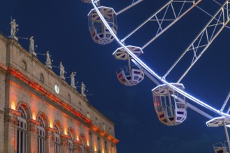 Ferris wheel cabins rotating over bayonne city hall illuminated in orange during christmas night in