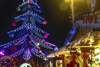 Luminous christmas tree towering over festive stalls adorned with lights and decorations at the