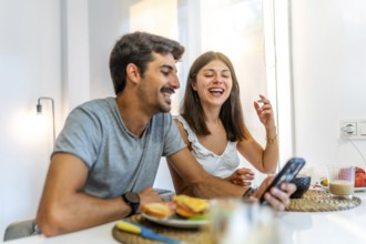 Young couple enjoying breakfast and having fun while using a smartphone in their modern kitchen