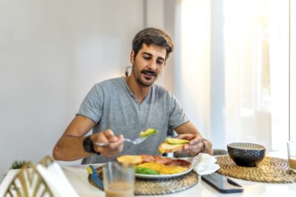 Man adding fresh avocado to toast while enjoying a healthy breakfast at home, embracing a balanced