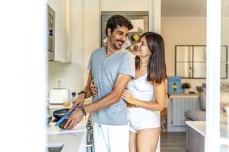 Romantic couple embracing while preparing a healthy breakfast together in a bright, modern kitchen,