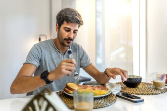 Young man enjoying breakfast with crispy bacon, fluffy eggs, toast, and steaming coffee in a