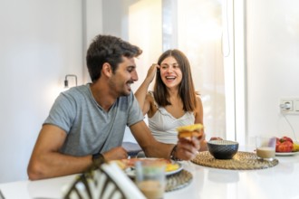 Young couple enjoying breakfast at home, laughing and sharing joyful moments together, creating a