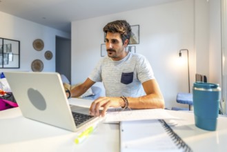 Young male freelancer concentrating on his laptop, working remotely from his modern home office