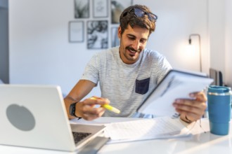 Young male freelancer comparing information on his tablet with data on his laptop, working from his