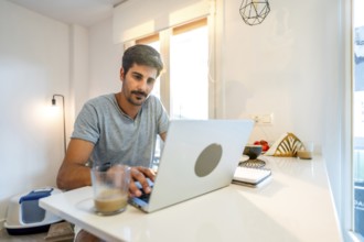 Young man concentrating on his laptop, enjoying a coffee while working remotely from his stylish
